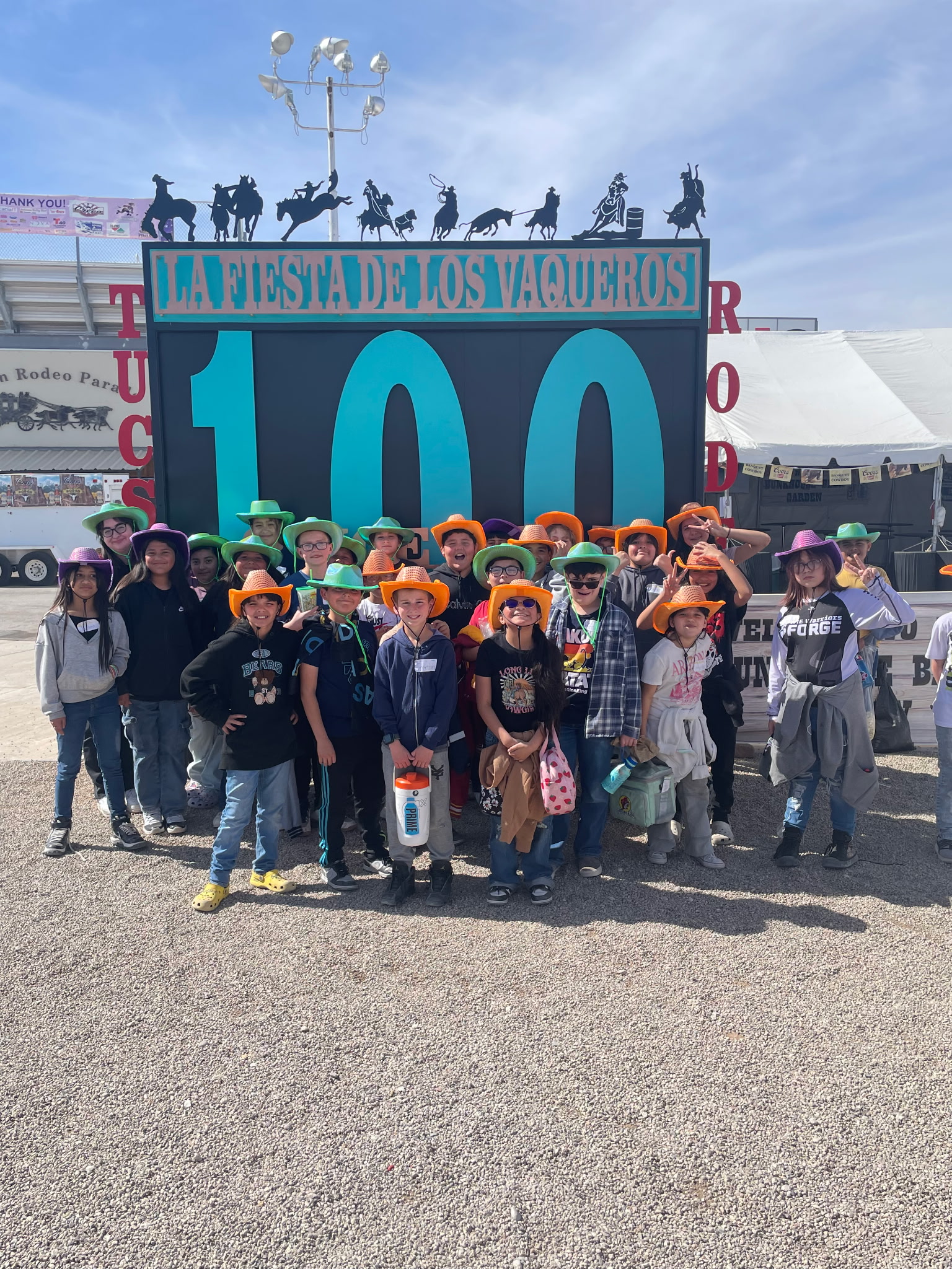 Students in colorful cowboy hats stand in front of the La Fiesta de los Vaqueros 100 sign