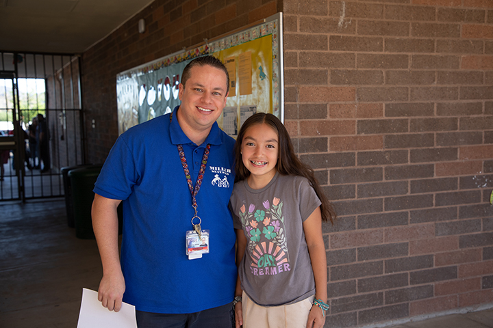 A teacher in a blue shirt poses with a girl in a brown shirt