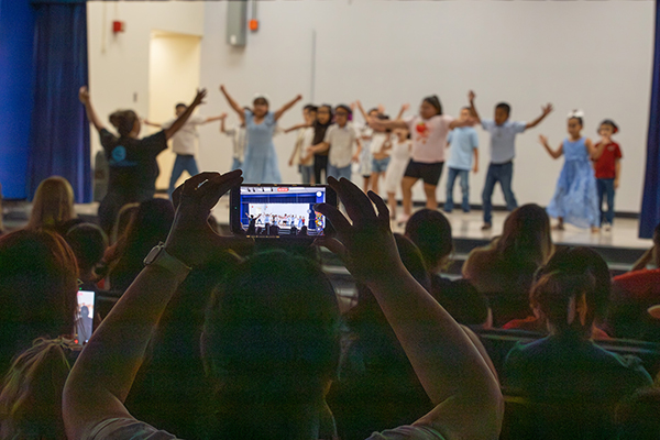 A parent holds a phone up to record the student performance