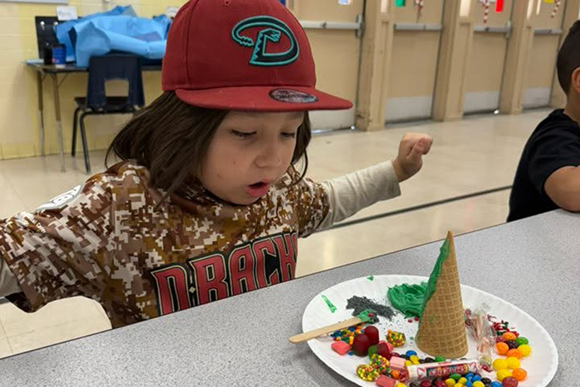A little boy in a Dbacks jersey and hat looks excitedly at his ice cream cone tree creation