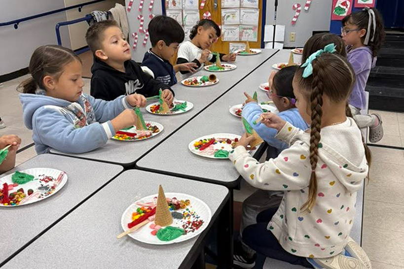 Students sit at a cafeteria table making their ice cream cone Christmas trees