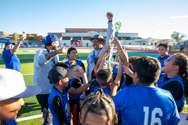 Students and their coach cheer as they hold up the trophy they won